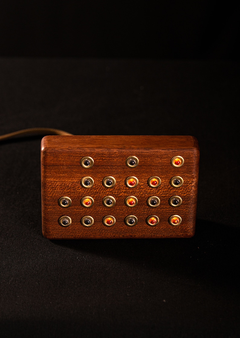 May include: A rectangular wooden box with multiple small, round buttons. The buttons are arranged in rows and columns, with some buttons having a red center and others a black center. The box has a brass-colored trim around each button.