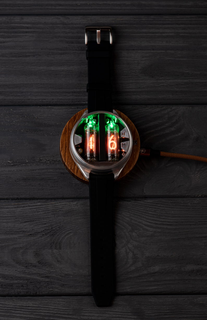 May include: A unique wristwatch featuring a round wooden base and a stainless steel case. The watch displays time with glowing orange and green numerals within glass tubes. It has a black leather strap and a silver buckle.