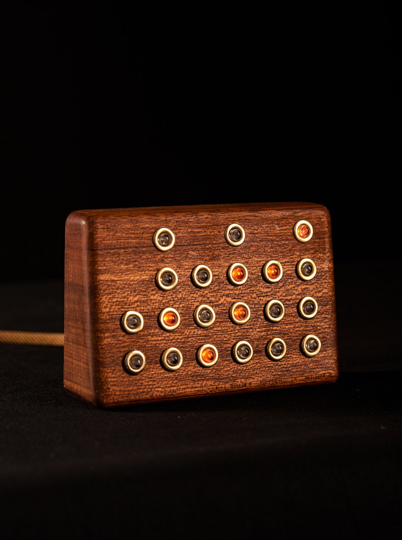 May include: A rectangular wooden object with a dark finish, featuring multiple small, circular buttons. Some buttons have amber-colored centers, while others are dark. The object is set against a black background.