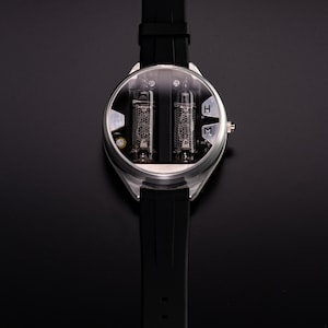 May include: A unique wristwatch with a black silicone band and a silver-colored case. The watch face features two visible vacuum tubes and a clear cover. The watch has a buckle clasp and is set against a black background.