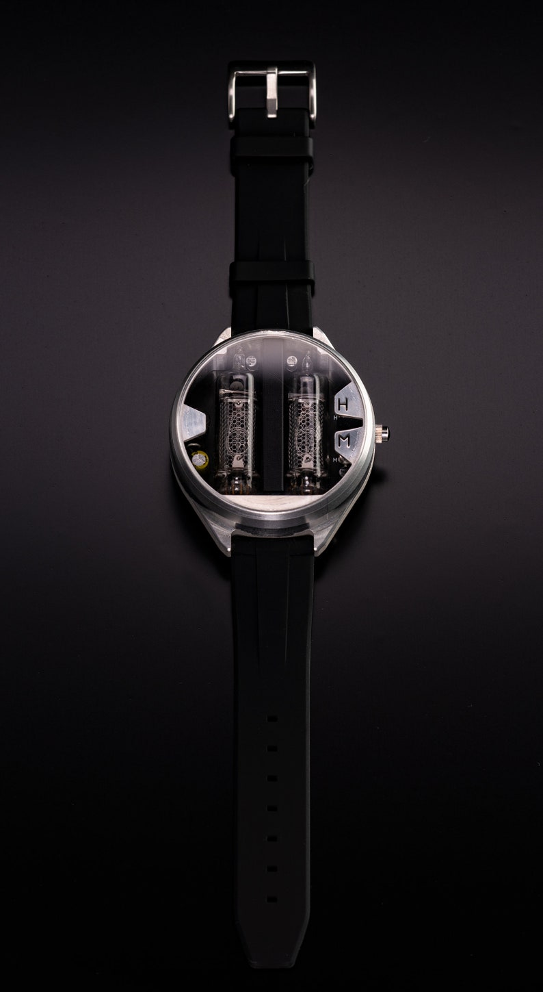May include: A unique wristwatch with a black silicone band and a silver-colored case. The watch face features two visible vacuum tubes and a clear cover. The watch has a buckle clasp and is set against a black background.