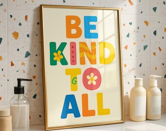 Könnte beinhalten: Ein gerahmter Kunstdruck mit den Worten "BE KIND TO ALL" in farbenfrohen, verspielten Buchstaben. Das Kunstwerk hat einen cremefarbenen Hintergrund und ist in einem goldenen Rahmen gefasst. Der Druck wird auf einer weißen Oberfläche mit Seifenspendern angezeigt.
