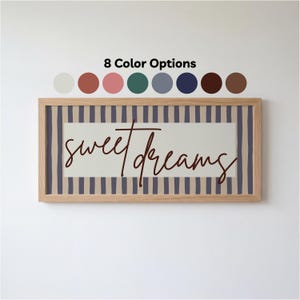 May include: A framed print with the words "sweet dreams" in a cursive font. The artwork features a beige background with vertical blue stripes and a wooden frame. Above the frame are eight colour options.