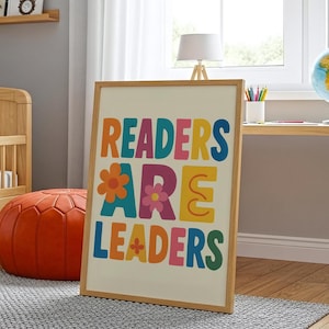 May include: A framed print with the words "READERS ARE LEADERS" in colourful, playful letters. The print features a cream background and a light wood frame. The letters are orange, blue, pink, purple, and yellow.
