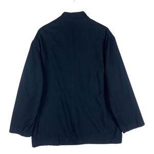 K&ouml;nnte beinhalten: Dunkelmarineblaue Jacke mit Stehkragen und langen &Auml;rmeln. Die Jacke ist aus einem einfarbigen, blickdichten Stoff gefertigt und h&auml;ngt an einem wei&szlig;en Kleiderb&uuml;gel. Die R&uuml;ckseite der Jacke ist sichtbar.