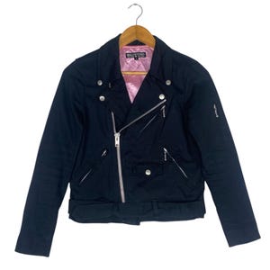 May include: Black biker-style jacket with a pink quilted lining, silver zippers, and snap closures. The jacket features an asymmetrical zip, a small pocket, and a waist belt. The brand name "HELL CAT PUNKS" is visible on the lining.