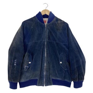 May include: A dark blue corduroy bomber jacket featuring a full-length silver zipper, a ribbed blue collar, and matching ribbed cuffs. The jacket includes two front pockets with silver snap buttons and a cream-colored sherpa lining inside.