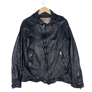 May include: Black leather jacket with a collared neckline, a zipper closure, and multiple zippered pockets. The jacket is hanging on a wooden hanger against a white background. The leather appears worn and textured.
