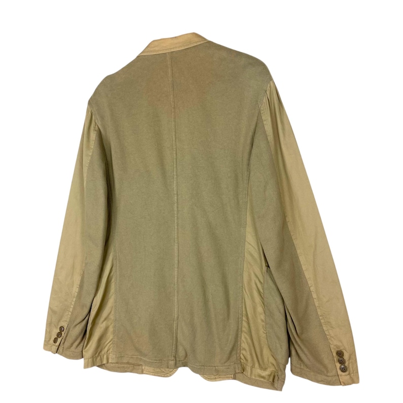 May include: A tan blazer with a two-button closure and a notched lapel. The jacket has a contrasting fabric on the sleeves and sides. The back of the blazer is visible, showing a center seam. The blazer is made of a soft, textured fabric.