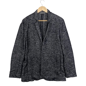 May include: A dark navy blue and white speckled blazer featuring a notched lapel, long sleeves, and a single-breasted front closure. The garment is constructed from a textured knit fabric and includes two side pockets, hanging on a wooden hanger.
