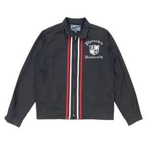May include: A black zip-up jacket featuring a collar, long sleeves, and two vertical stripes in red and white running down the front. The chest displays a white shield emblem with the text Pherrow's University in a gothic-style font.