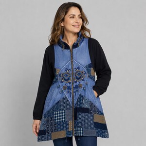 Op de afbeelding: Een jack met ritssluiting, zwarte lange mouwen en een blauw voorpand in denimstijl. De voorkant toont een centraal bloemenborduurwerk omringd door een patchworkpatroon van diverse blauwe en beige geometrische prints en een hoge kraag.