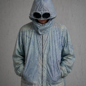 May include: A light blue jacket with a hood and built-in goggles. The jacket has a full-length zipper and a subtle, textured pattern. The hood is up, obscuring the face. The jacket appears to be made of a lightweight material.