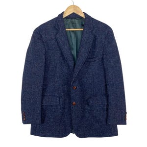 May include: A navy blue blazer with a textured, speckled pattern, featuring a notched lapel, two front buttons, two flap pockets, and three buttons on each sleeve cuff. The interior is lined with a solid dark green fabric and hangs on a hanger.