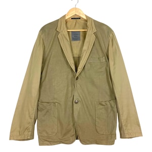 May include: A tan blazer with a two-button closure, two front pockets, and a notched lapel. The jacket is hanging on a wooden hanger. The sleeves are a lighter shade of tan than the body of the jacket.
