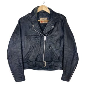 May include: Black leather jacket with a notched collar, asymmetrical zipper closure, and multiple zippered pockets. Features a belt with a buckle at the waist. The jacket is hanging on a wooden hanger.