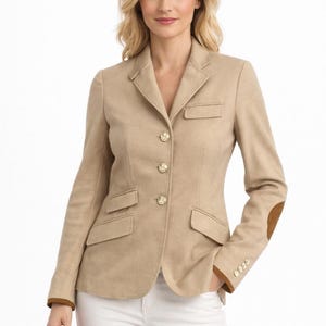 Puede incluir: Blazer beige con botones dorados y coderas marrones. La chaqueta tiene dos bolsillos delanteros y un bolsillo en el pecho. La modelo lleva pantalones blancos. Un estilo clásico.