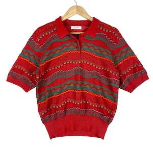 May include: A red short-sleeved polo shirt with a colorful, patterned design. The shirt features a collared neckline and a three-button placket. The pattern includes horizontal stripes in green, brown, orange, and purple.