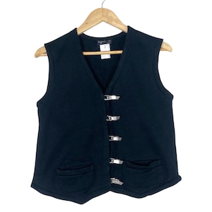 May include: A black sleeveless vest featuring a V-neckline and a front closure with five silver-toned metal buckles. The garment includes two front patch pockets and a white brand label at the inner neckline with the number 2 printed on it.