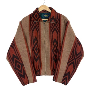 May include: A zip-up jacket featuring a textured brown, rust orange, and dark brown geometric pattern. The garment has a high collar, long sleeves, and a full-length front zipper. The interior is lined with a dark green fabric and includes a label.