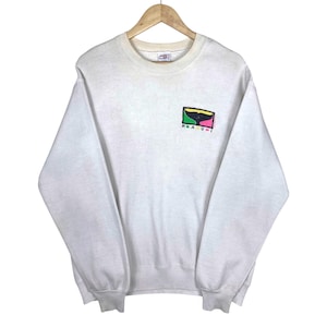 May include: A vintage white sweatshirt with a crew neck and long sleeves. The sweatshirt features a colorful graphic of a whale tail and the word "MAUI" in a rectangular design. The garment is displayed on a wooden hanger.