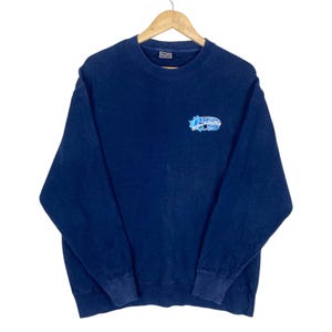 May include: Navy blue sweatshirt with a crew neck and long sleeves. The sweatshirt features a light blue and white graphic on the upper left chest that reads "Paces". The cuffs and hem are ribbed.