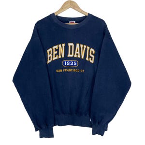 May include: Navy blue Ben Davis sweatshirt with the brand name in a gold arched font. Below the name is "1935" in a blue circle and "SAN FRANCISCO CA" in gold. The sweatshirt is hanging on a wooden hanger.