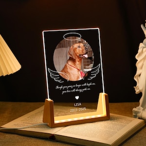 May include: A personalised memorial light featuring a photo of a dog, a halo, and wings. The text reads "Though your paws no longer walk beside me, your love will always guide me." The light also includes the name "LISA" and the dates "2015-2025".