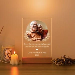 Könnte beinhalten: Personalisiertes LED-Nachtlicht mit einem Foto eines älteren Paares. Das Licht hat einen Holzsockel und eine transparente Acrylplatte mit dem Text "LOVE YOU MOM & DAD 2025". Das Licht strahlt warm.