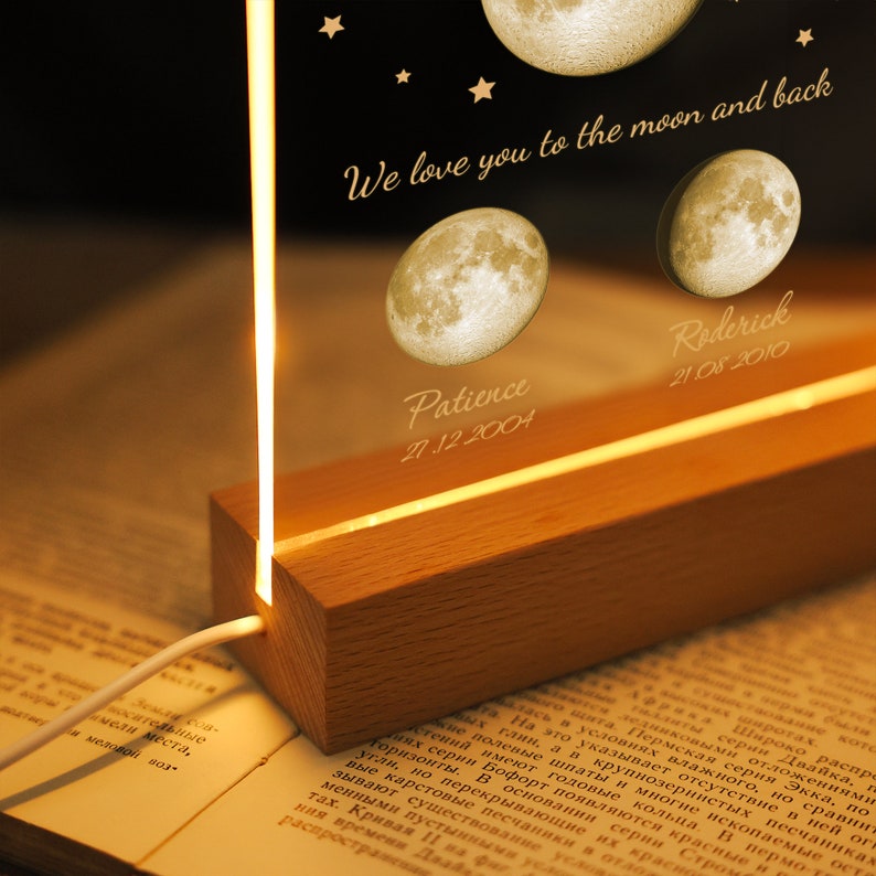 Pode incluir: Luz noturna personalizada com base de madeira e painel acr&iacute;lico transparente. O painel &eacute; gravado com ilustra&ccedil;&otilde;es de luas, nomes, datas e a frase "We love you to the moon and back."
