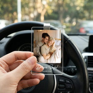 May include: A rectangular clear acrylic car visor clip featuring a printed photograph of a couple embracing. The bottom of the transparent plaque displays the white text Drive Safe! I LOVE YOU. The item includes a silver metal clip at the top.