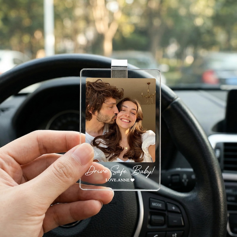 May include: A rectangular clear acrylic car rearview mirror charm featuring a printed photograph of a couple. The text "Drive Safe. Baby!" and "LOVE.ANNE" with a heart symbol is printed in white script at the bottom of the transparent plaque.