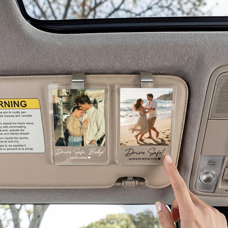 May include: Two rectangular clear acrylic photo clips attached to a car sun visor. The left clip shows a couple embracing with the text Drive Safe Baby! LOVE-ANNE. The right clip shows a couple on a beach with the text Drive Safe! ALWAYS WITH YOU.