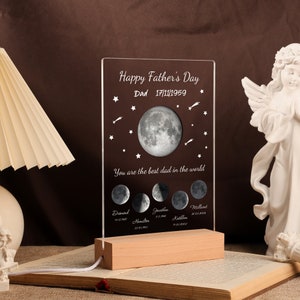 Pode incluir: Um presente personalizado para o Dia dos Pais com um painel de acr&iacute;lico transparente com um design de fases da lua e o texto "Happy Father's Day Dad 17/11/1959". O painel est&aacute; sobre uma base de madeira com um cabo de alimenta&ccedil;&atilde;o. O texto "You are the best dad in the world".