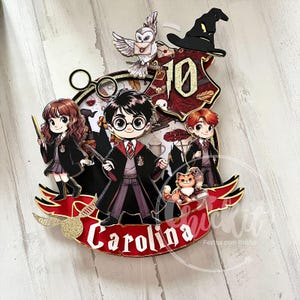 Puede incluir: Un adorno para tarta colorido con personajes de dibujos animados de una serie de fantasía. El diseño incluye un sombrero de mago, un búho y el número 10. El nombre "Carolina" se muestra en una pancarta roja con detalles dorados.