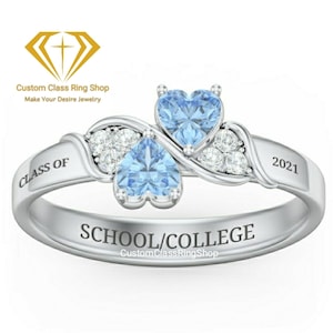 Puede incluir: Anillo de plata con dos piedras azules en forma de corazón y una banda que dice "CLASS OF 2021 SCHOOL/COLLEGE CustomClassRingShop"