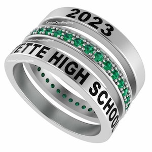Op de afbeelding: Zilveren klasring met een band van groene smaragdstenen. De ring heeft de tekst "2023" op de bovenste band en "ETTE HIGH SCHOOL" op de onderste band.
