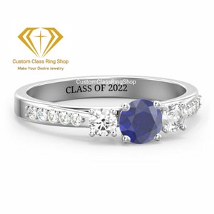 May include: A silver ring with a blue sapphire and white diamonds. The ring is engraved with "CustomClassRingShop CLASS OF 2022".