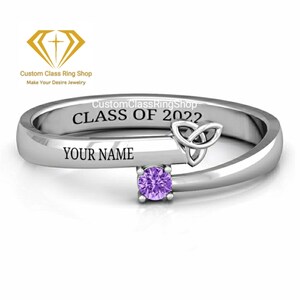 May include: A silver ring with a purple gemstone, a Celtic knot design, and the engraved text "CLASS OF 2022" and "YOUR NAME". The ring is from Custom Class Ring Shop.
