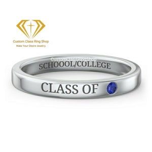 May include: A silver ring with the words "CLASS OF" and "SCHOOOL/COLLEGE" engraved on it. A small, round, blue gemstone is set into the ring. The ring is a graduation or class ring.