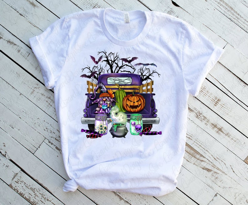 K&ouml;nnte beinhalten: Ein wei&szlig;es T-Shirt mit einem lila Pickup, der eine Hexe, einen K&uuml;rbis und einen Kessel transportiert. Der Truck ist mit Halloween-Dekorationen geschm&uuml;ckt, darunter Flederm&auml;use, Spinnweben und S&uuml;&szlig;igkeiten.