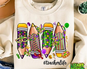 May include: A cream colored sweatshirt with a design of four pencils in Mardi Gras colors. The pencils are decorated with purple, green, and gold beads, masks, and fleur-de-lis. The text "#teacherlife" is printed below the pencils.
