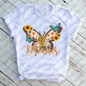 May include: White t-shirt featuring a colourful butterfly design. The butterfly has a leopard print body and is surrounded by sunflowers. The word "Dreamer" is written in orange and yellow letters below the butterfly.