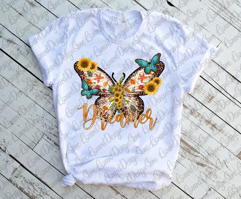 May include: White t-shirt featuring a colourful butterfly design. The butterfly has a leopard print body and is surrounded by sunflowers. The word "Dreamer" is written in orange and yellow letters below the butterfly.