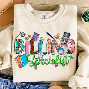 Könnte beinhalten: Ein beiger Pullover mit dem Text "Billing Specialist" in bunten Buchstaben, umgeben von Büroartikeln wie einem Taschenrechner, einem Laptop, einem Hefter und einem Stift.