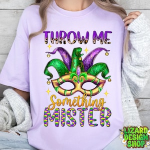 May include: Purple t-shirt featuring a green, purple and gold Mardi Gras mask with the text "Throw Me Something Mister".
