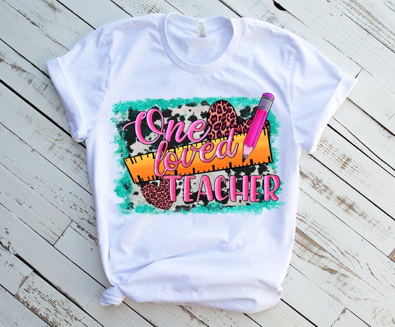 Puede incluir: Camiseta blanca con un dise&ntilde;o gr&aacute;fico que dice "One loved teacher" con un l&aacute;piz rosa y una regla, estampado de leopardo y estampado de vaca.