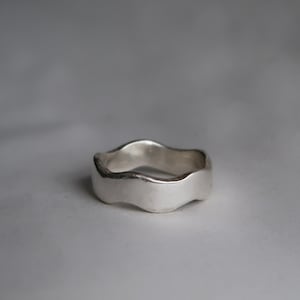 May include: A silver ring with a wavy, organic design. The ring has a smooth, polished surface and a thick band. The ring is a simple yet elegant piece of jewellery, suitable for everyday wear.
