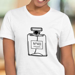 Puede incluir: Camiseta blanca con un dibujo lineal negro de un frasco de perfume y el texto "N°40 ORIGINAL". La camiseta es de cuello redondo y la lleva una persona.