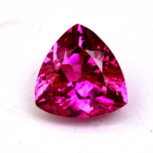 Pode incluir: Uma gema rosa vibrante com um corte triangular, mostrando um brilho brilhante e facetas intrincadas.